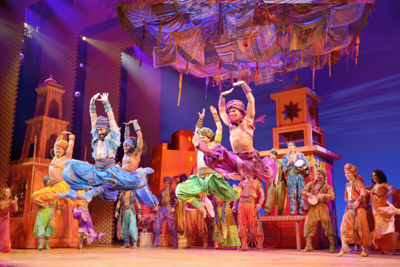 The cast of Aladdin on Broadway. A group of people wearing colorful clothing performing Arabian Nights.